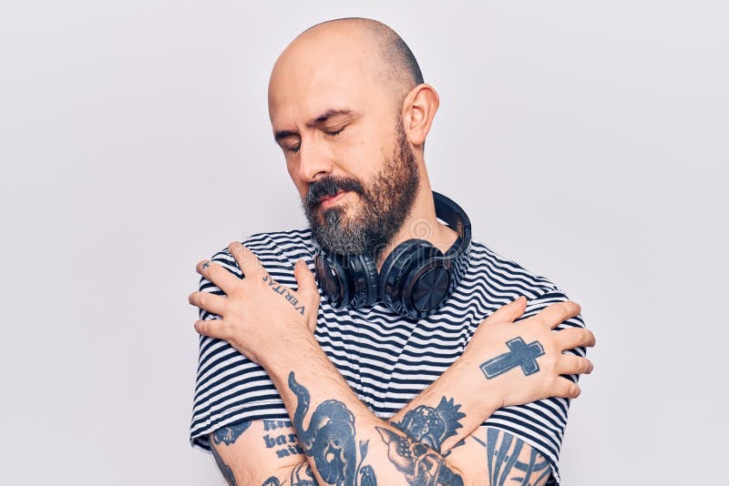 Ung, stilig man som lyssnar på musik med hörlurar som kramar sig själv, glad och positiv, leende självsäker fotografering för bildbyråer