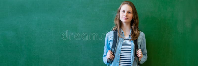 Ung säker le kvinnlig högstadiumstudent som framme står av den svart tavlan i klassrum och att bära en ryggsäck