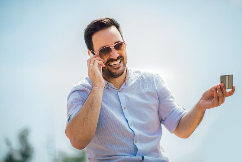 Ung tillf?llig utomhus- maninnehavmobiltelefon och kreditkort royaltyfri foto Ung tillf?llig utomhus- maninnehavmobiltelefon och kreditkort royaltyfri foto