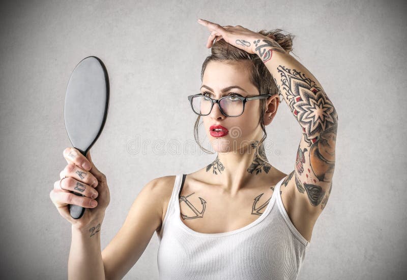 Young beautiful tough women with lots of tattoos looking herself in the mirror. Young beautiful tough women with lots of tattoos looking herself in the mirror