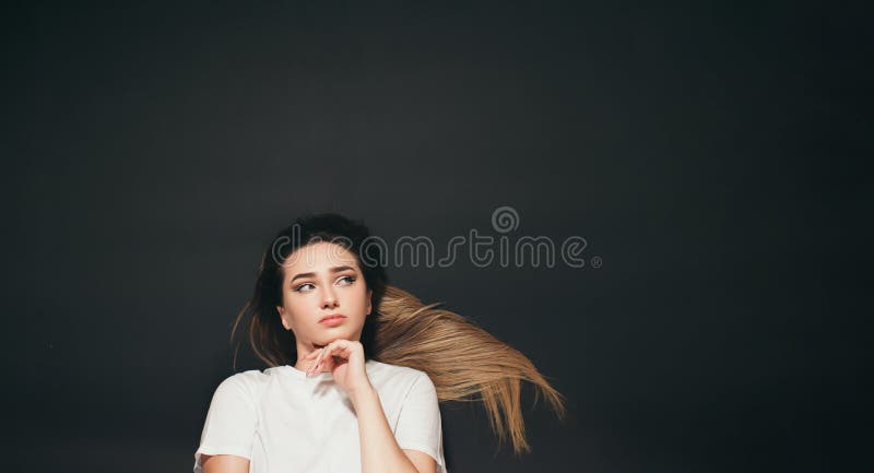 Ung tänkande kvinna med långt hår som ligger på svart bakgrund, förvirrad flickvy arkivfoto