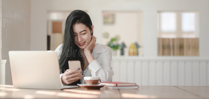 Ung vacker affärskvinna som använder sin smartphone när hon arbetar med sitt projekt royaltyfri foto