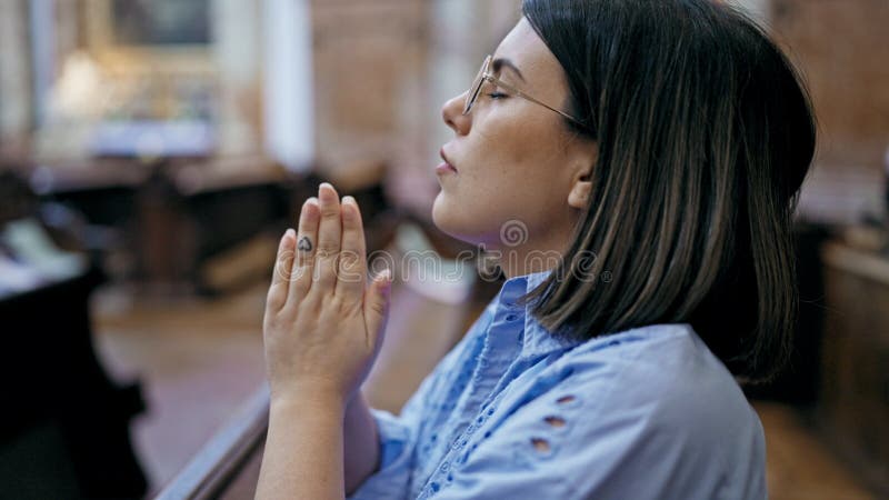 Ung, vacker historisk kvinna som ber på en kyrkobänk på st. karl borromacurren us kyrka