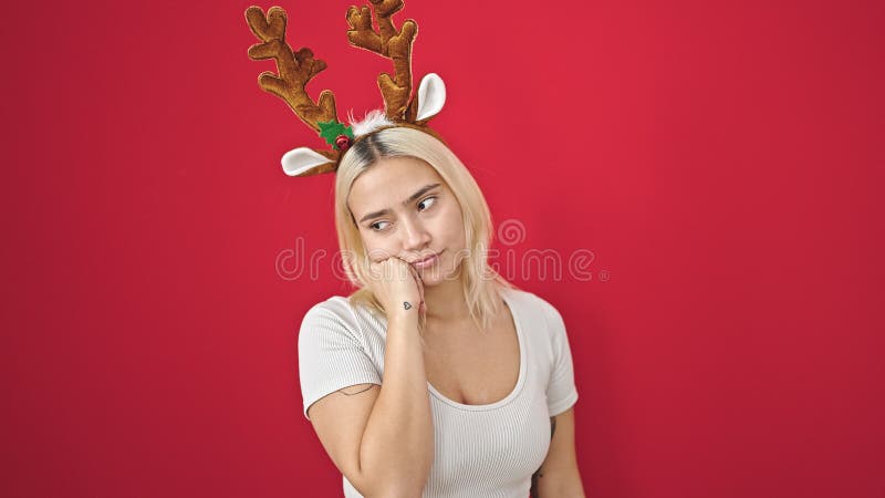 Ung, vacker historisk kvinna som bär reindeer christmas-hatt med tvivel över isolerad röd bakgrund royaltyfri fotografi