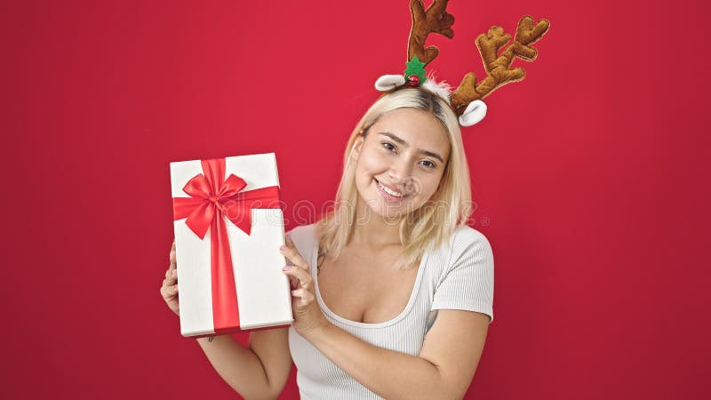 Ung, vacker historisk kvinna som bär renhästar christmas som håller gåva över isolerad röd bakgrund arkivbilder