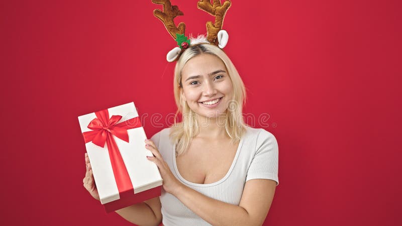 Ung, vacker historisk kvinna som bär renhästar christmas som håller gåva över isolerad röd bakgrund royaltyfri fotografi