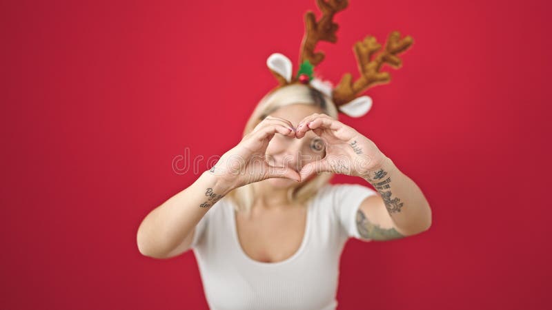 Ung, vacker historisk kvinna som bär renhästar, julklappare som gör en hjärtgest över isolerad röd bakgrund royaltyfria bilder