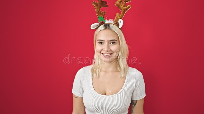 Ung, vacker historisk kvinna som leker självsäker med reindeer christmas-hatt över isolerad röd bakgrund fotografering för bildbyråer