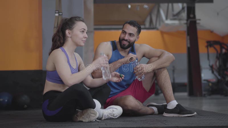 Ung vacker kaukasisk kvinna och stilig medelöstman som chattar på gym och dricksvatten. stark stock video