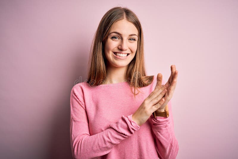 Ung, vacker rödbrun kvinna som bär tillfällig tröja över isolerad rosa bakgrund och applåderar glad och glad. Ung, vacker rödskallig kvinna som bär en tillfällig tröja över isolerad rosa bakgrund och applåderar lyckliga och glädjande leende stolta händer tillsammans