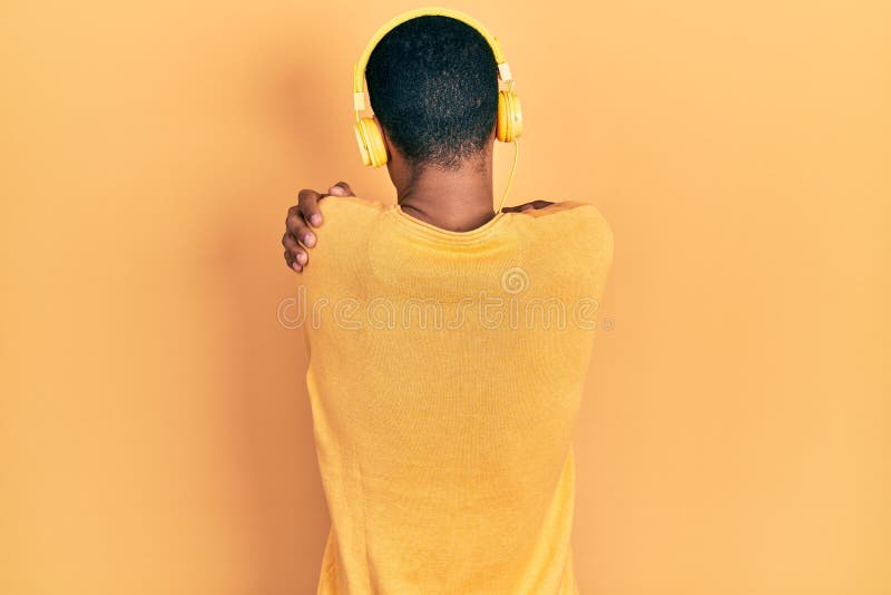 Unga afrikaner som lyssnar på musik med hörlurar som kramar sig själva lyckliga och positiva bakifrån arkivbild