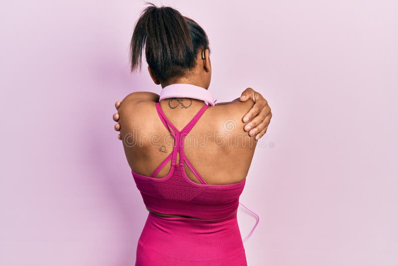 Unga afrikanska amerikanska flickor som bär gym kläder och använder hörlurar som kramar sig själva lyckliga och positiva bakifrån royaltyfri fotografi