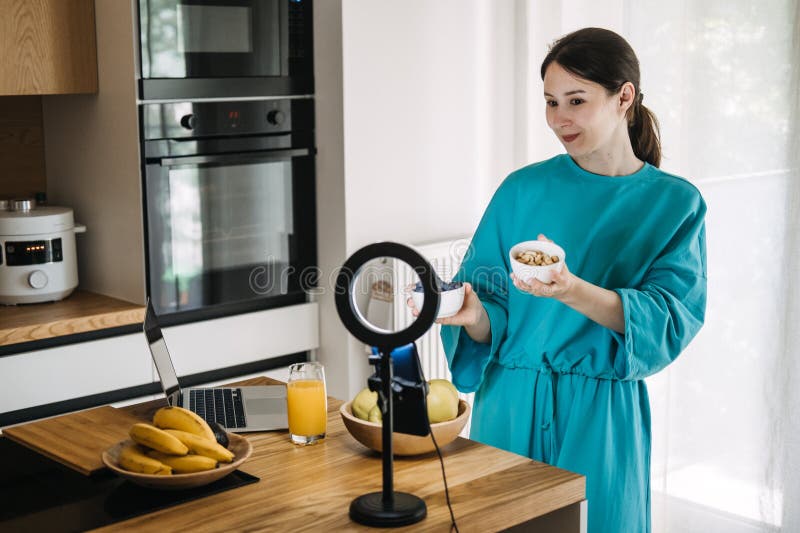 Unga asiatiska kvinnor filmar hälsosamt matinnehåll med smartphone och ring light i köket. Skapad ekonomi och välfärd arkivbilder