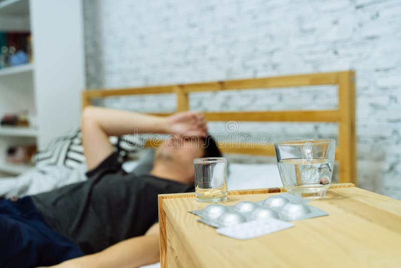 Unga asiatiska män som känner sig sjuka och som ligger på sängen med mediciner och tabletter på bordet
