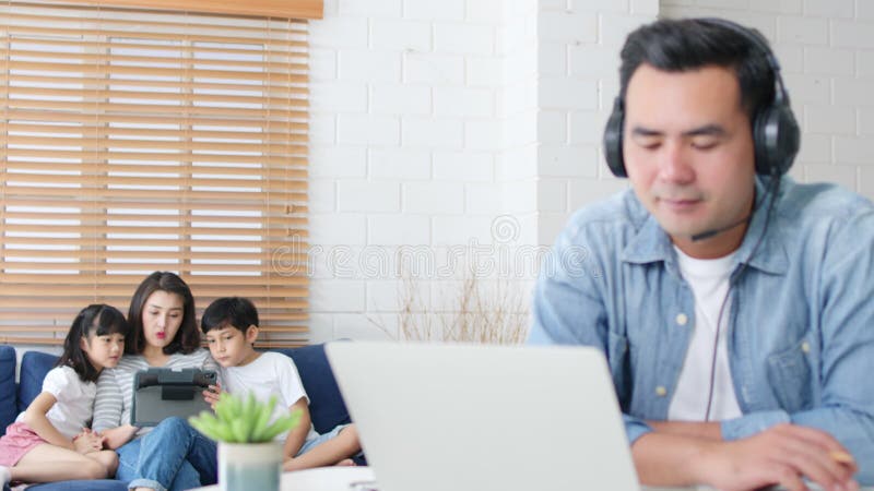 Unga asiatiska pappor arbetar hemma med familjens moderdotter och son sitter tillsammans på soffsoffan. ny normal livsstil