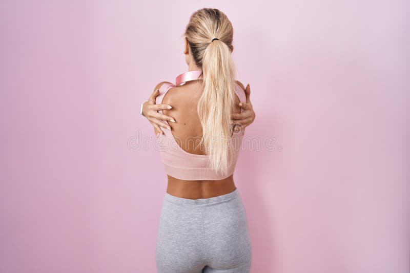 Unga blonda kvinnor som bär sportkläder och hörlurar som kramar sig själva, glada och positiva bakifrån arkivbilder