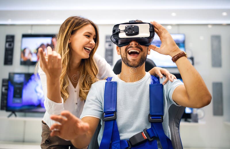 Unga, glada par som spelar videospel med virtuellt verklighetsglas i den tekniska butiken arkivfoton