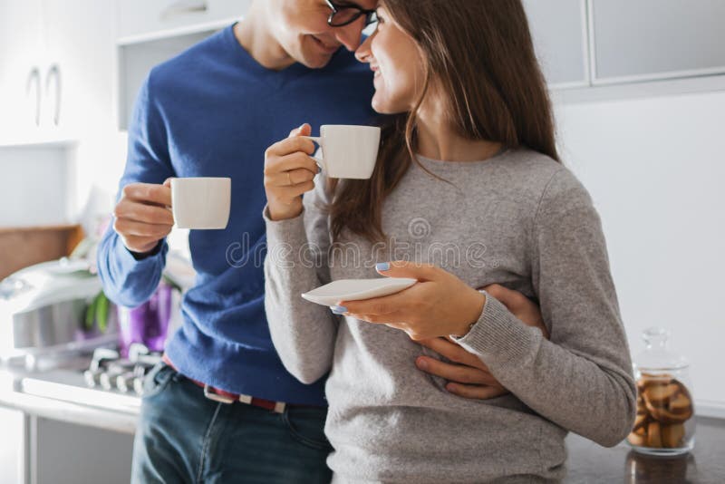 Unga gulliga par som kramar och dricker te i k?ket royaltyfri fotografi Unga gulliga par som kramar och dricker te i k?ket royaltyfri fotografi