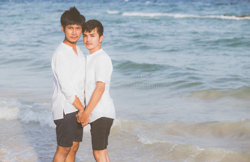 Unga homosexuella, unga asiatiska par som står tillsammans på stranden på sommaren, som homosexuella handhänder som går till havs arkivbilder Unga homosexuella, unga asiatiska par som står tillsammans på stranden på sommaren, som homosexuella handhänder som går till havs arkivbilder