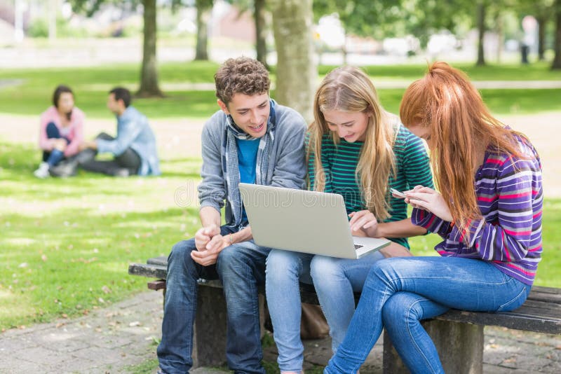 Unga högskolestudenter som använder bärbara datorn parkerar in royaltyfri fotografi Unga högskolestudenter som använder bärbara datorn parkerar in royaltyfri fotografi
