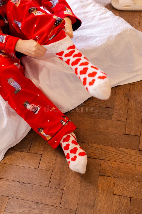 Unga kvinnor i rött pyjamas som pendlar på konstiga strumpor med röda hjärtan. tjej som gör sig redo hemma i sovrummet arkivfoton