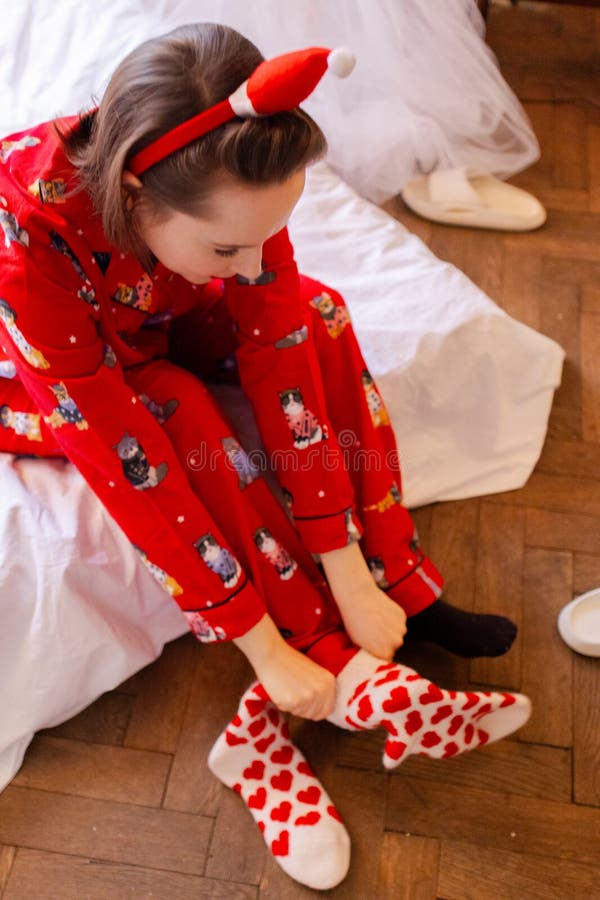 Unga kvinnor i rött pyjamas som pendlar på konstiga strumpor med röda hjärtan. tjej som gör sig redo hemma i sovrummet royaltyfria bilder