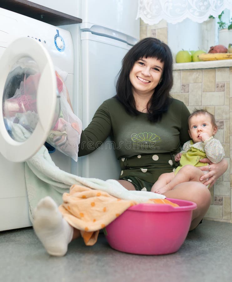 Young women with baby putting clothes in to washing machine and smiling. Young women with baby putting clothes in to washing machine and smiling