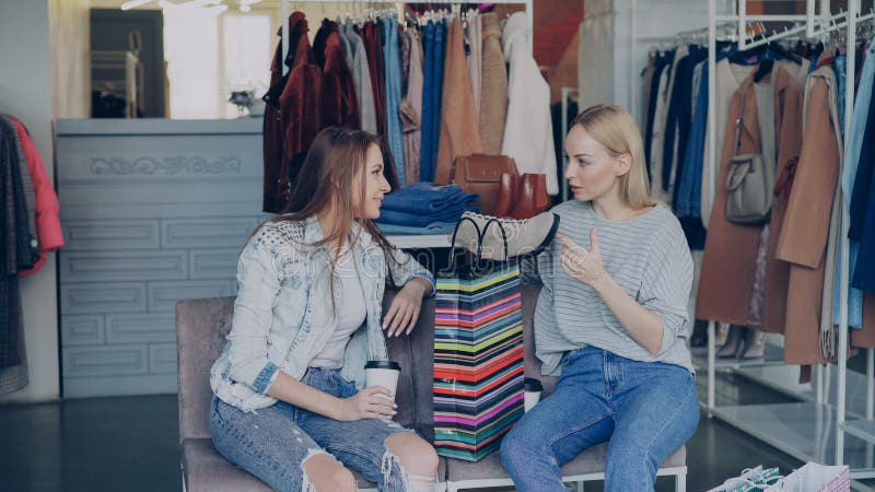 Unga kvinnor som diskuterar köpta ankelskor medan de vilar i boutique. Flickor är entusiastiska över att shoppa. arkivbilder