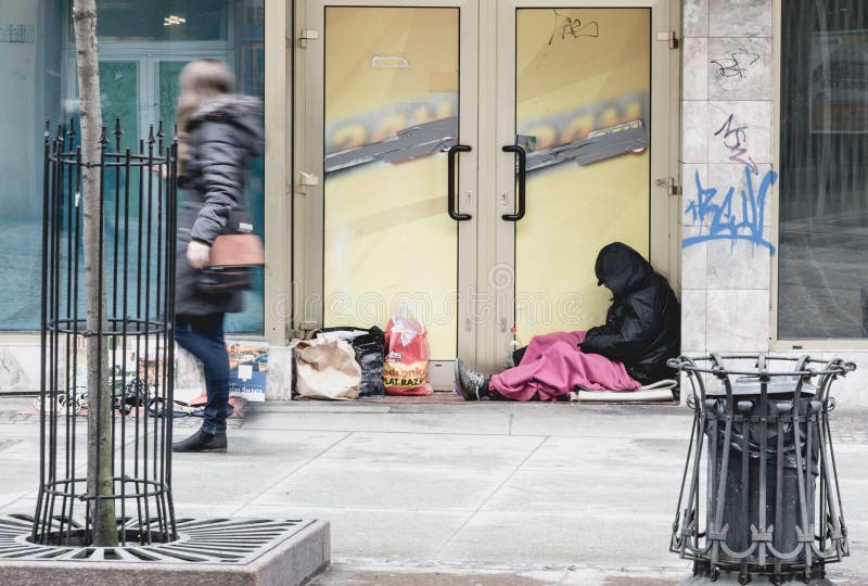 Young women passing homeless man siting in cold weather at closed door shop in Wroclaw, Poland. Young women passing homeless man siting in cold weather at closed door shop in Wroclaw, Poland