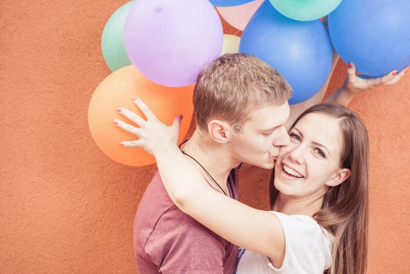 Unga lyckliga par nära den orange väggen står med ballonger arkivfoto Unga lyckliga par nära den orange väggen står med ballonger arkivfoto