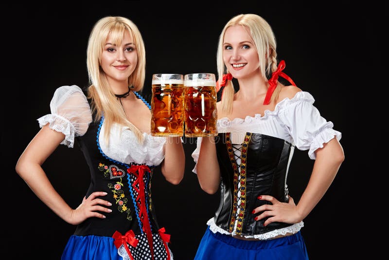 Unga och härliga bavarianflickor med öl två rånar på svart bakgrund royaltyfria foton Unga och härliga bavarianflickor med öl två rånar på svart bakgrund royaltyfria foton