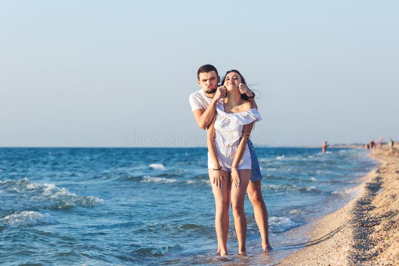 Unga par gör en framsida och att ha gyckel på stranden royaltyfri fotografi Unga par gör en framsida och att ha gyckel på stranden royaltyfri fotografi