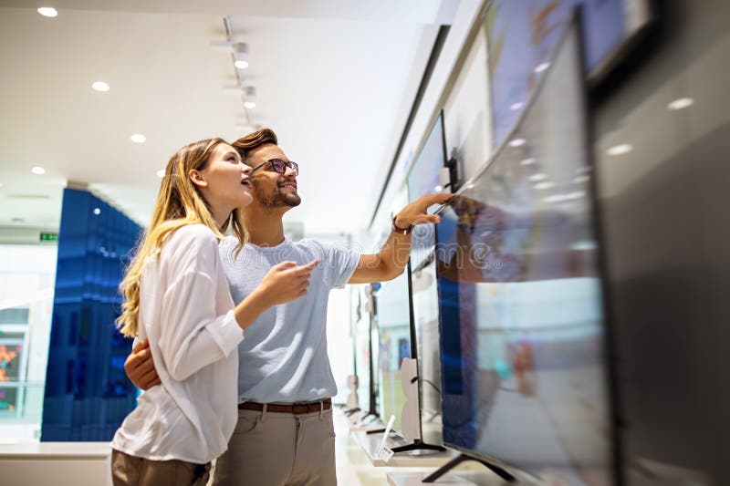Unga par i hemelektronikbutiken som tittar på den senaste digitala televisionen. arkivfoto