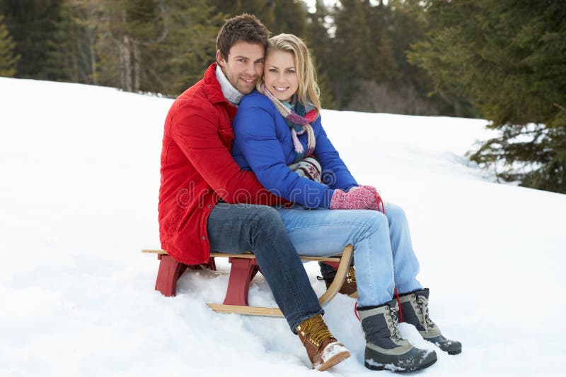 Young Couple On A Sled In Alpine Snow Scene smiling at camera. Young Couple On A Sled In Alpine Snow Scene smiling at camera