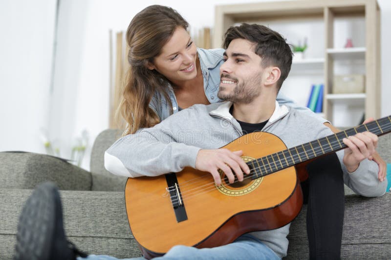 Unga par som spelar gitarr på soffa inomhus arkivfoton