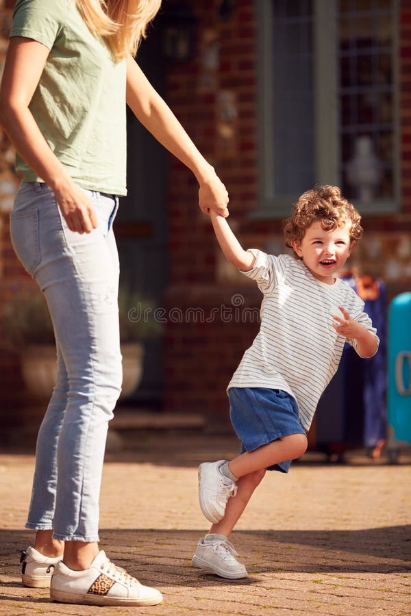 Young Boy Holding Mothers Hand Outside House As They Leave For Family Vacation. Young Boy Holding Mothers Hand Outside House As They Leave For Family Vacation