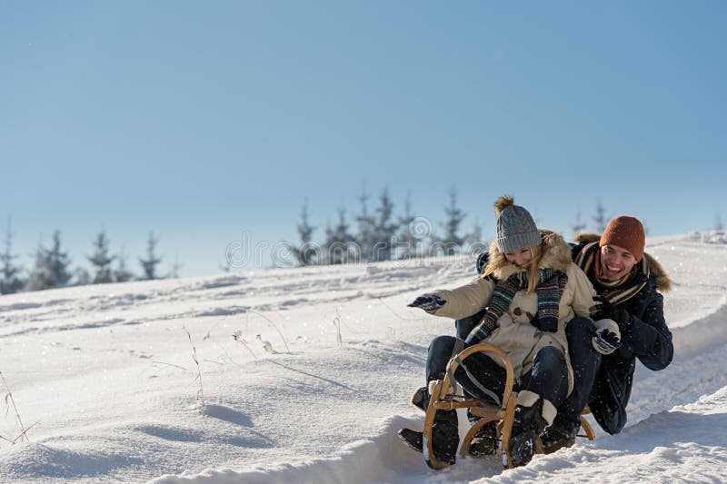 Young playful couple having fun in the snow sledging downhill. Young playful couple having fun in the snow sledging downhill