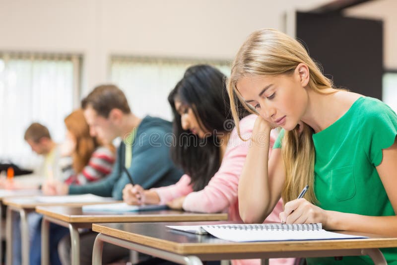 Unga studenter som skriver anmärkningar i klassrum royaltyfri foto Unga studenter som skriver anmärkningar i klassrum royaltyfri foto
