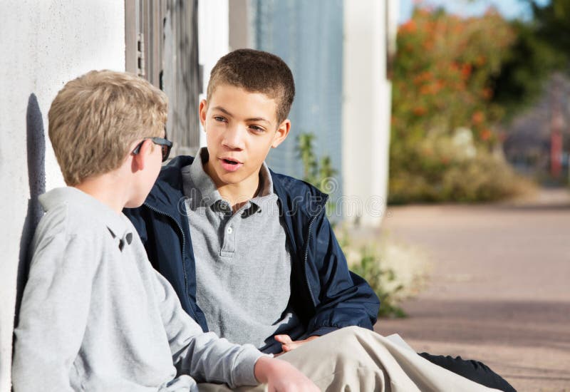 Teen male talking to friend seated outside on ground. Teen male talking to friend seated outside on ground