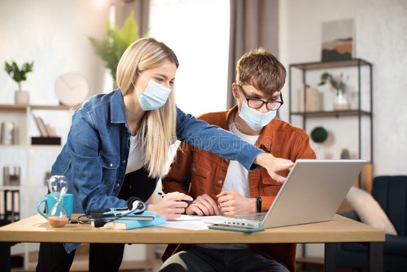 Unga vänner i ansiktsmasker samarbetar eller arbetar på distans online från hemmet fotografering för bildbyråer