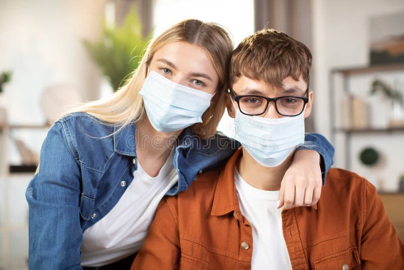 Unga vänner i ansiktsmasker som sitter på kameran och sitter vid bordet och använder bärbar dator arkivbilder