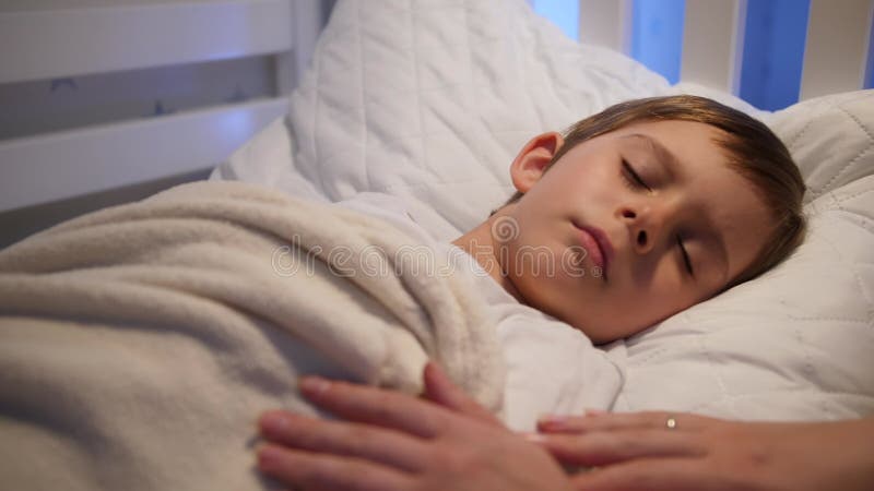 Unga vårdande mor som stramar och kysser hennes sovande lilla son på natten. Begreppet föräldraskap och familjelycka. arkivfilmer