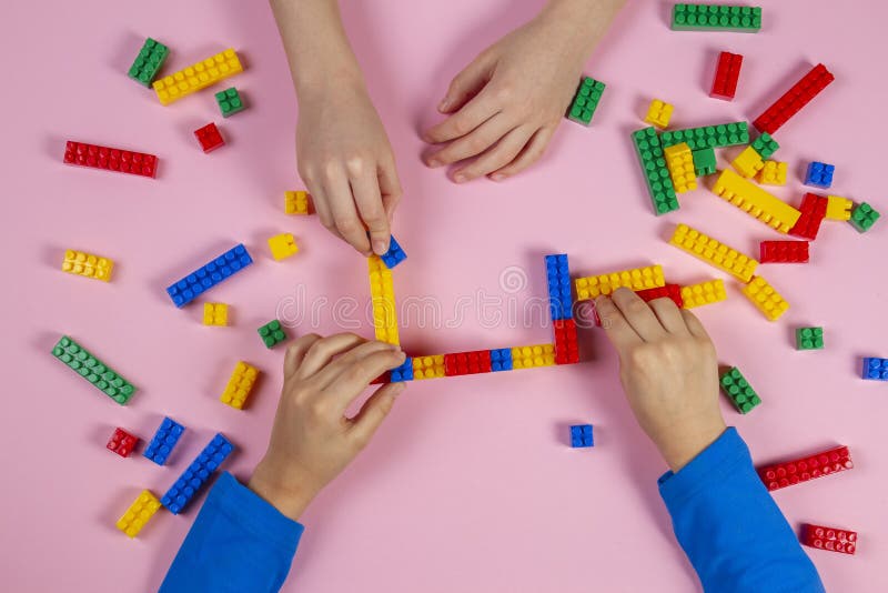 Ungar som spelar med plast- tegelstenar för färgrik byggnad på rosa bakgrund Bildande framkallande leksakerbakgrund fotografering för bildbyråer Ungar som spelar med plast- tegelstenar för färgrik byggnad på rosa bakgrund Bildande framkallande leksakerbakgrund fotografering för bildbyråer