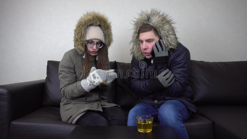 Young people sit at home on the devan in the triggers because of the cold in the house. A man calls on the phone and asks for help. Unpaid heating bills. 4k. Young people sit at home on the devan in the triggers because of the cold in the house. A man calls on the phone and asks for help. Unpaid heating bills. 4k