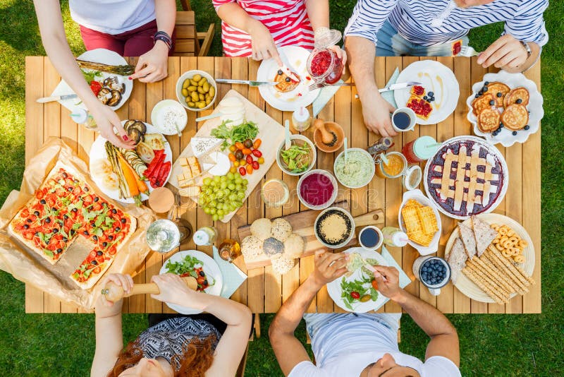 Young people eating pizza, fruit, bread, pies, cookies and vegetables outside. Young people eating pizza, fruit, bread, pies, cookies and vegetables outside