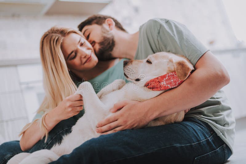 Ungdomliga kyssande par som omfamnar deras halkande hund arkivbild Ungdomliga kyssande par som omfamnar deras halkande hund arkivbild