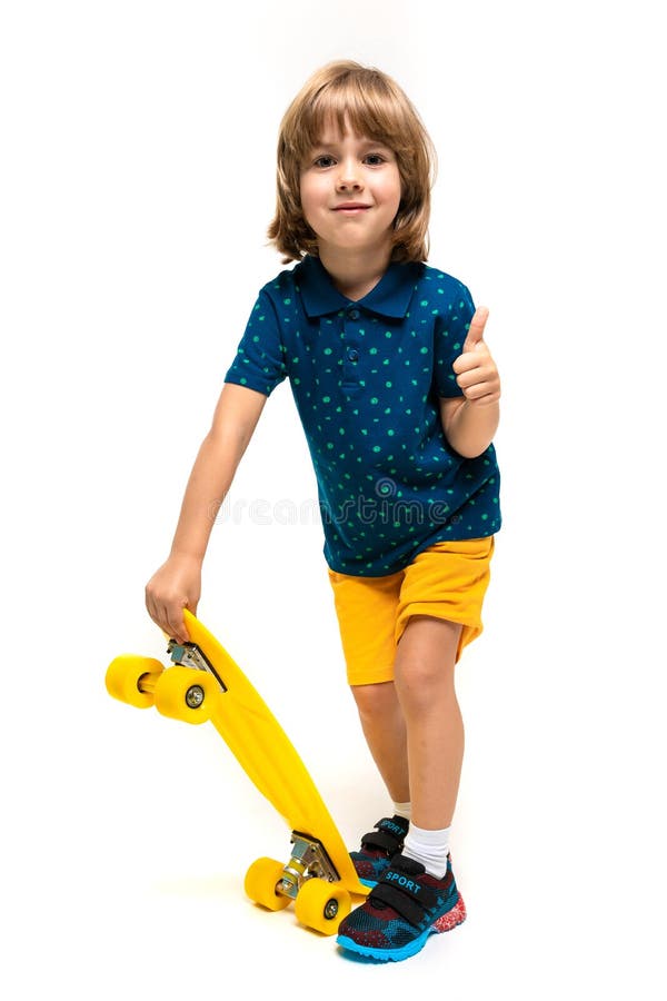 Ungefär europeisk söt pojke i sportkläder står och håller en gul skateboard i händerna på en vit bakgrund. fotografering för bildbyråer