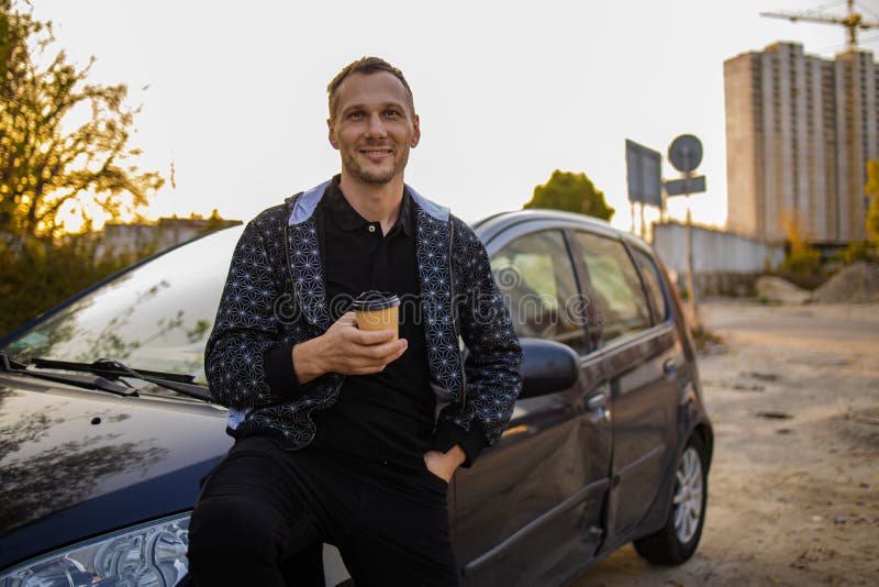 Ungefär glad man dricker kaffe nära bilen arkivbilder