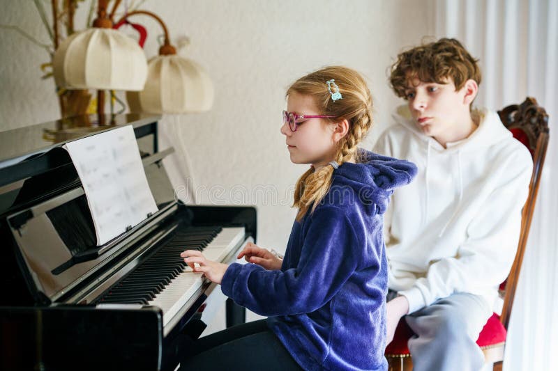 Ungefär skolflicka som utövar piano medan en tonårspojke lyssnar uppmärksamt. Barndom i musikinlärning royaltyfria foton