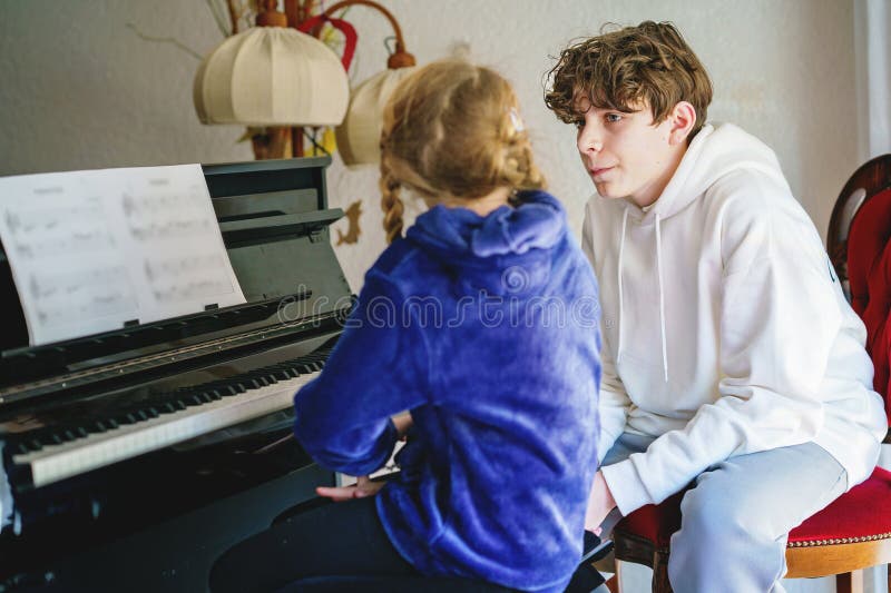 Ungefär skolflicka som utövar piano medan en tonårspojke lyssnar uppmärksamt. Barndom i musikinlärning royaltyfria bilder